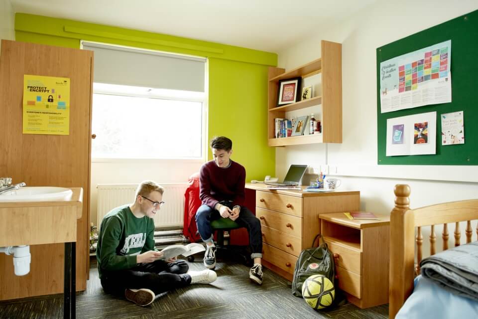 Two students sitting in accommodation room, one on the floor and one on a chair.